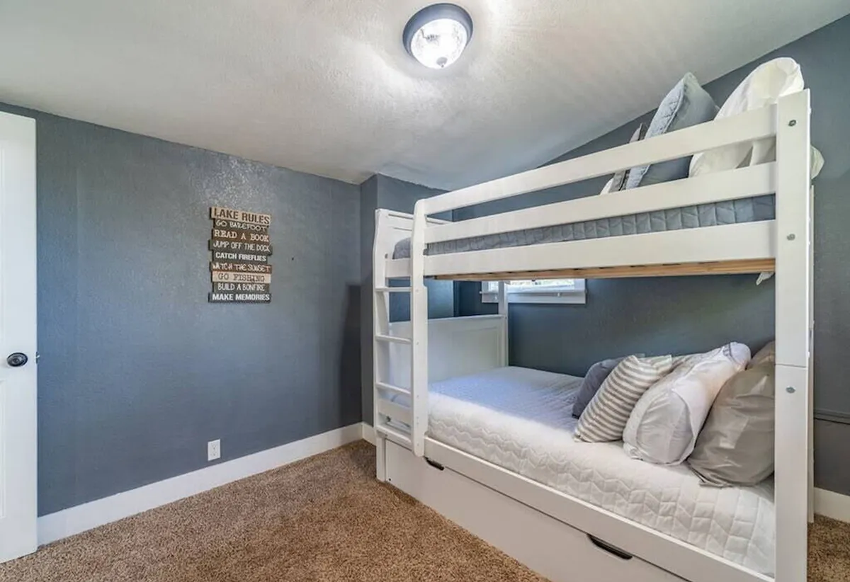 A bedroom with a bunk bed setup, decorative wall sign, and a window that brings in daylight. The space feels playful yet cozy, offering an ideal spot for children’s sleepovers or family accommodations.