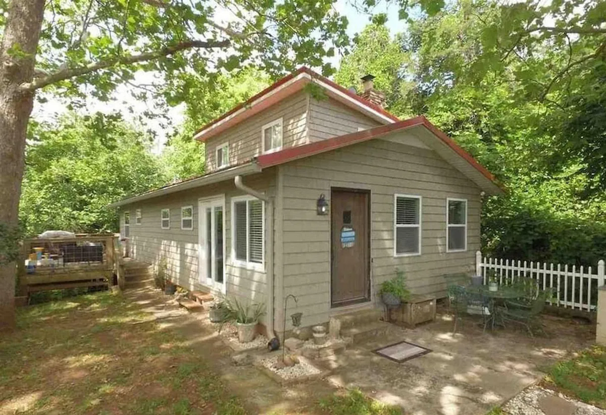 This image features the charming exterior of 950 Coveside Way, highlighted by a red roof, an inviting front door, and lush greenery surrounding the property. The porch and yard offer a welcoming space for families and groups to gather and relax outdoors.
