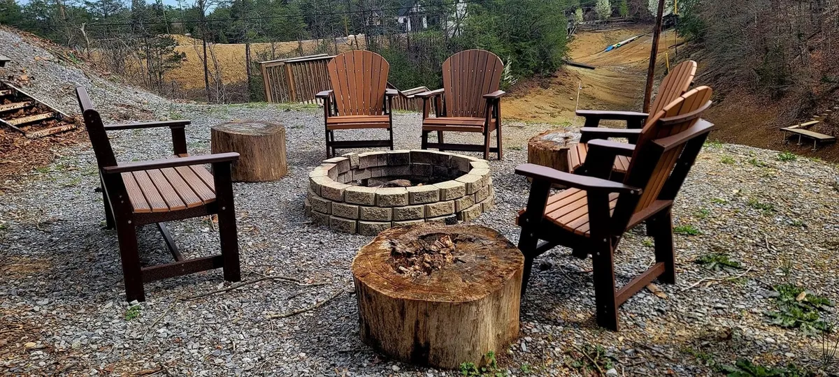 A classic fire pit is encircled by Adirondack chairs and rustic stump seating, creating an inviting space for gatherings, storytelling, and roasting marshmallows.