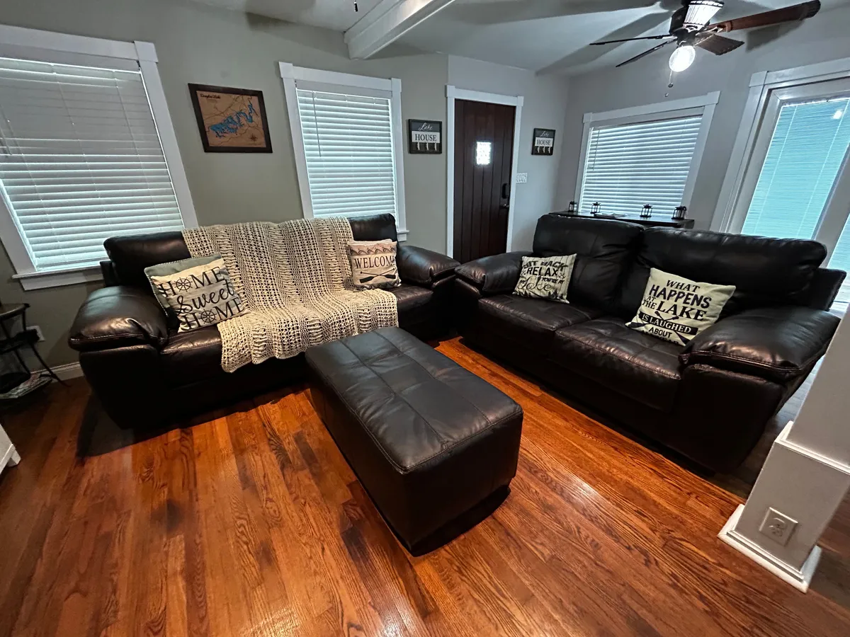 This image features a living room with leather sofas, a knitted throw blanket, decorative pillows, and a wooden floor. The arrangement suggests a cozy spot for relaxing, socializing, or watching TV. The atmosphere is welcoming and comfortable, ideal for gatherings.