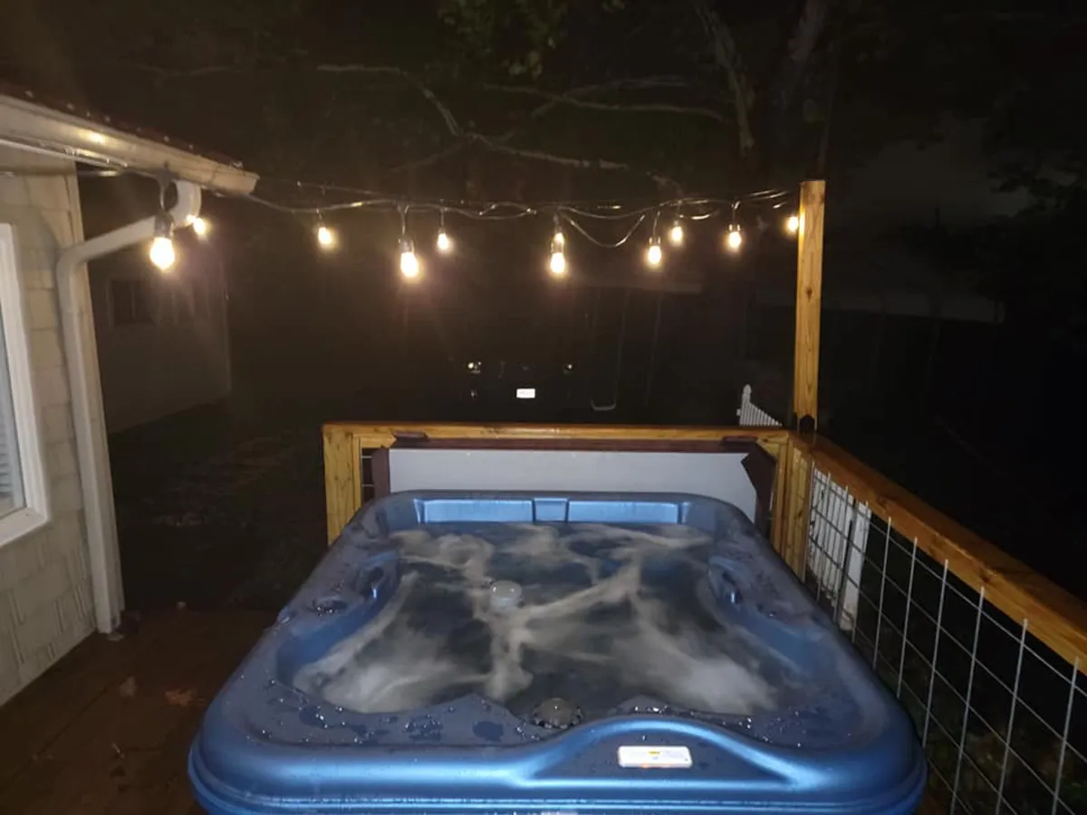 This image showcases a private hot tub on a wooden deck, surrounded by string lights. The natural backdrop and inviting setup emphasize relaxation and a tranquil outdoor experience, especially at night.